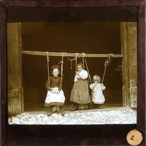 Three girls sitting on swings in door of barn or similar building