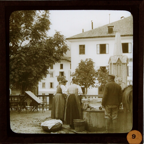Two women and man talking by fountain in village square