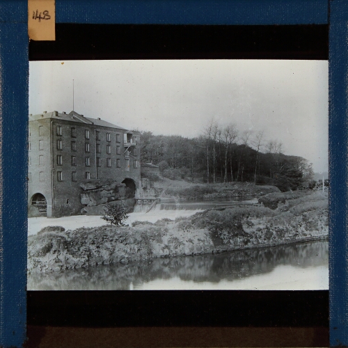 Factory with water wheel by side of weir in river