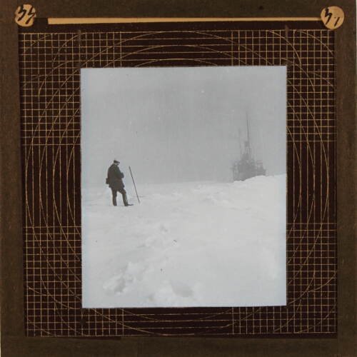 Man standing on snow with steamship in background