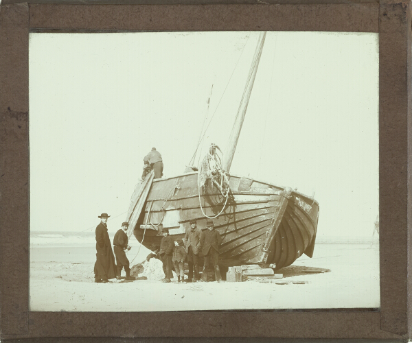 Priest and group of boys and men standing by boat on beach