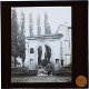 [Woman with luggage at archway at the entrance of cemetery  or church yard]