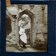[Woman in rural costume standing in doorway of ruined building]