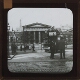 Horse-drawn tram waiting outside large building with columns – Front view of slide