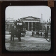 Horse-drawn tram waiting outside large building with columns – Rear view of slide