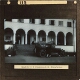 [Woman standing by motor car in front of arcaded building]