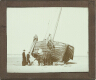 [Priest and group of boys and men standing by boat on beach]