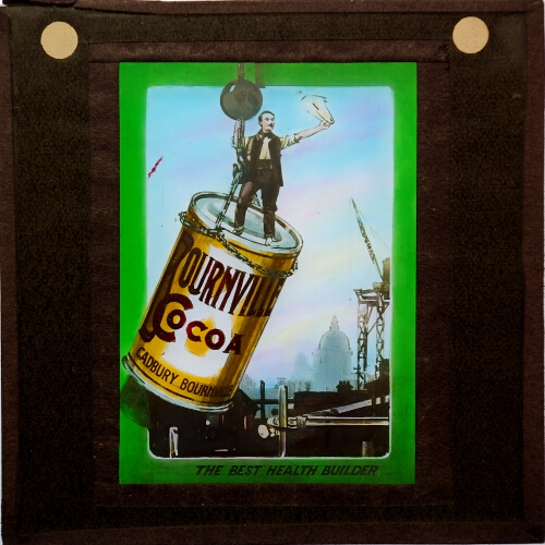 Workman on oversized cocoa tin carried by crane