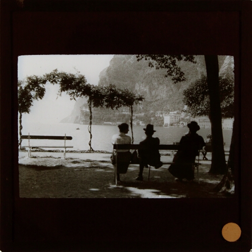 Three people sitting on park bench overlooking lake