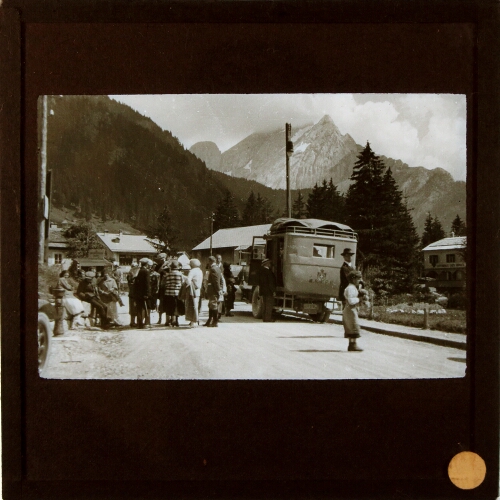 Group of people standing by motor bus in street in mountainous landscape