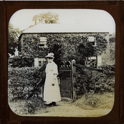 Woman standing at garden gate of large house