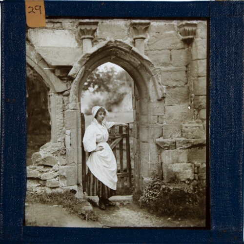 Woman in rural costume standing in doorway of ruined building
