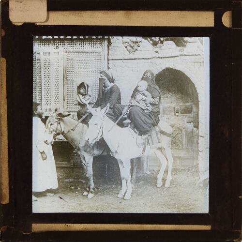 Two Arab women riding donkeys with children