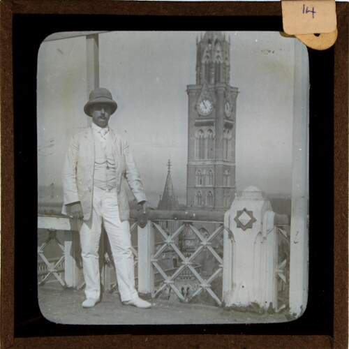 Man wearing colonial helmet posing with Rajabai Clock Tower in background