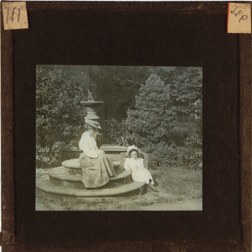 Woman and girl sitting on base of sundial in garden