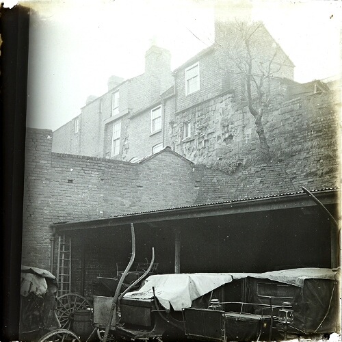 Photograph of shed with carriages, houses above