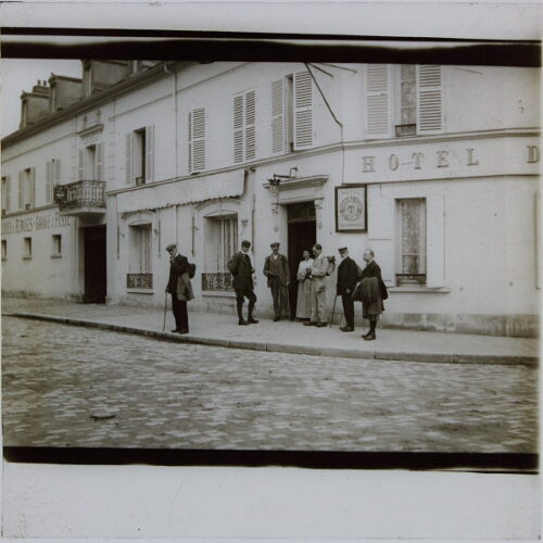 Group of men standing outside hotel in French town or village