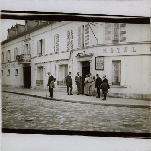 Group of men standing outside hotel in French town or village