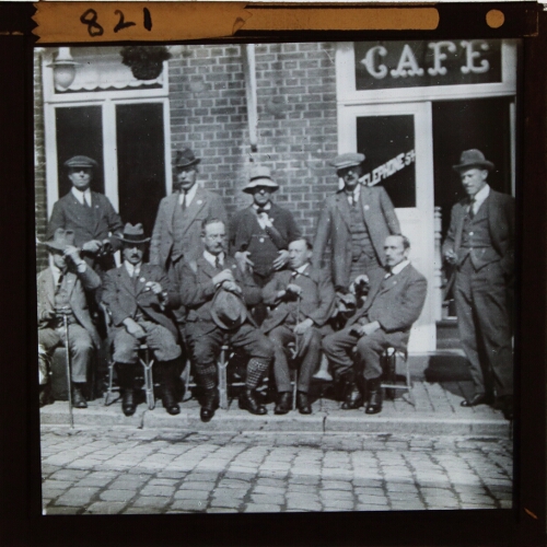 Group of men sitting and standing outside cafe in French town or village