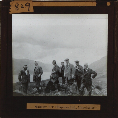 Group of men with walking sticks on top of hill overlooking lake