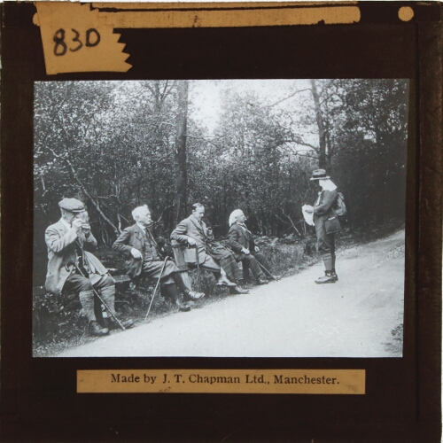 Group of men with walking sticks resting by side of road
