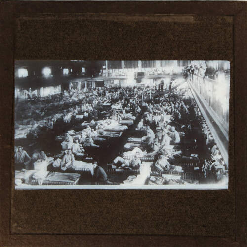 Large number of men resting on beds in large hall