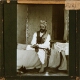 slide image -- [J.R. Halliday sitting on bed with water-pipe]